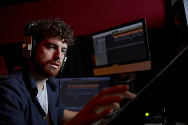 Man working in music studio using computer wearing head phones - MINF16228