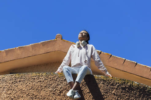 Junge Frau schaut weg, während sie an einem sonnigen Tag auf dem Dach sitzt - JRVF01008