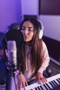Musikerin singt durch ein Mikrofon, während sie im Studio Klavier spielt - JRVF01016
