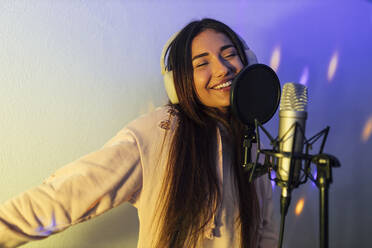 Smiling female singer with arms outstretched singing in studio - JRVF01023