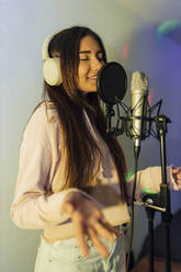 Young female singer with eyes closed gesturing while singing at studio - JRVF01024