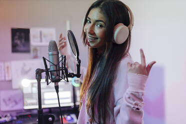 Smiling female singer wearing headphones gesturing while singing in studio - JRVF01028