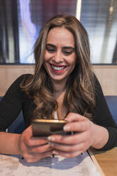 Glückliche Frau benutzt Mobiltelefon im Restaurant - JRVF01034