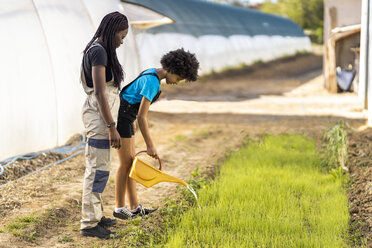 Female farmer looking at girl watering plants at organic farm - OIPF01035