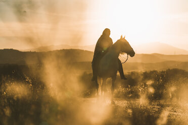 Frau reitet bei Sonnenuntergang auf einem Feld - DAMF00798