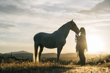 Frau küsst Pferd, während sie bei Sonnenuntergang auf einem Feld steht - DAMF00800