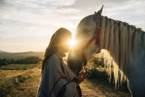 Woman embracing horse on field during sunset - DAMF00802