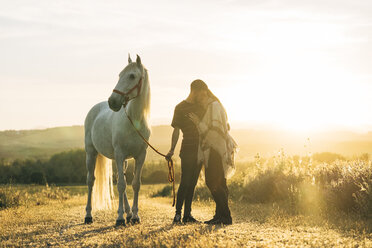 Verliebtes Paar mit Pferd auf einem Feld bei Sonnenuntergang - DAMF00805
