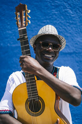 Lächelnder Mann mit Gitarre vor blauer Wand stehend - OCMF02138