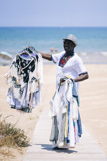 Männlicher Verkäufer verkauft Kleidung auf der Promenade am Strand - OCMF02140