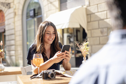 Lächelnde Frau, die ein Mobiltelefon benutzt, während sie in einem Straßencafé sitzt - EIF01195
