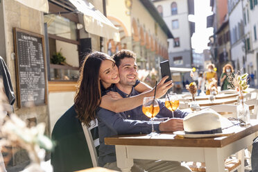 Tourist couple taking selfie through mobile phone at sidewalk cafe - EIF01203