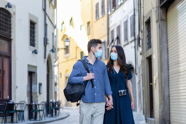 Touristenpaar mit Gesichtsschutzmaske, das sich auf einer Straße in der Stadt an den Händen hält - EIF01224