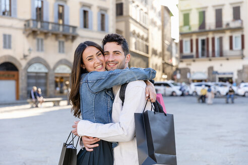 Lächelndes Touristenpaar, das Einkaufstüten hält und sich in der Stadt umarmt - EIF01242