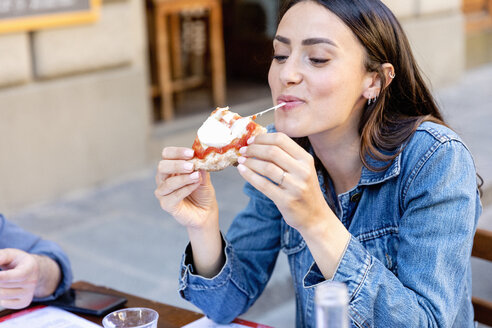 Smiling woman eating pizza at sidewalk cafe - EIF01249