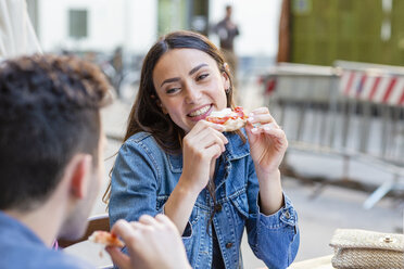 Junge Frau mit Pizzastück lächelt und sieht einen Mann an - EIF01250