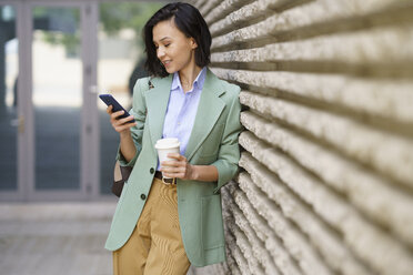 Businesswoman using smart phone while leaning on wall - JSMF02299