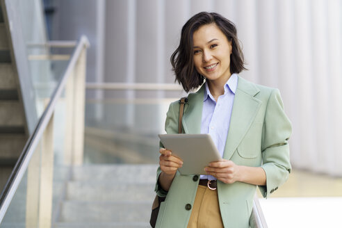 Lächelnde weibliche Fachkraft mit digitalem Tablet in einem Bürogebäude - JSMF02303