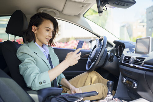 Weibliche Berufstätige, die im Auto sitzend ein Smartphone benutzen - JSMF02309