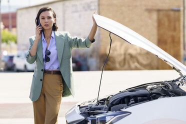 Businesswoman talking on smart phone by broken down car - JSMF02313