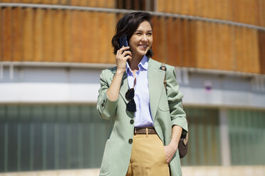 Lächelnde Geschäftsfrau, die wegschaut, während sie mit einem Smartphone telefoniert - JSMF02316