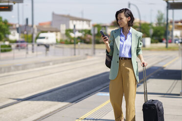 Weibliche Fachkraft, die ihr Smartphone benutzt, während sie am Bahnhof auf einen Zug wartet - JSMF02322