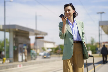 Geschäftsfrau sendet Sprachnachricht über Smartphone am Bahnhof - JSMF02327