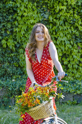 Lächelnde schöne Frau auf dem Fahrrad sitzend mit einem Korb voller Freesienblüten im Garten - EIF01262