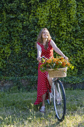 Happy young woman sitting on bicycle in front of hedge while looking away - EIF01266