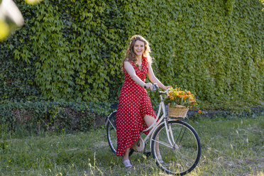 Fröhliche Frau auf dem Fahrrad sitzend an einer Efeuhecke im Garten - EIF01269