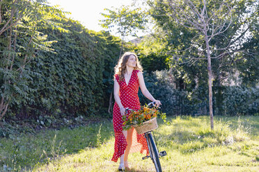 Young woman wheeling bicycle in garden while looking away - EIF01272