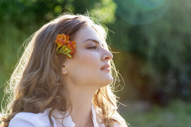 Beautiful young woman with blond hair wearing freesia flower looking away - EIF01290