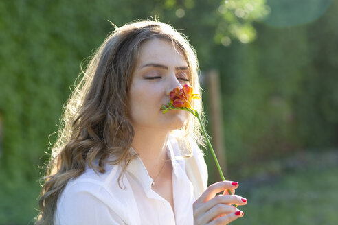 Junge Frau mit geschlossenen Augen riecht an einer Freesienblüte an einem sonnigen Tag - EIF01291