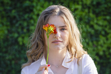 Beautiful young woman covering eye with freesia flower during sunny day - EIF01293
