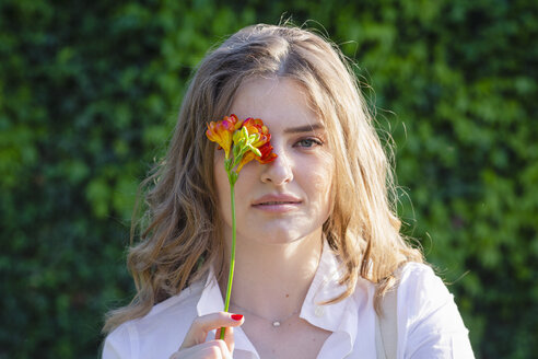 Schöne junge Frau bedeckt ihr Auge mit einer Freesienblüte an einem sonnigen Tag - EIF01293