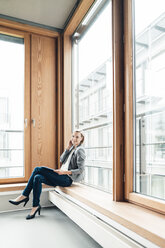 Smiling businesswoman sitting with legs crossed at knee on window sill - JOSEF04783