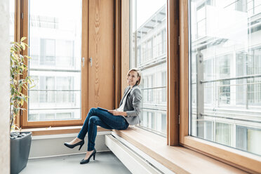 Geschäftsfrau mit digitalem Tablet, die sich im Büro an ein Fenster lehnt - JOSEF04785