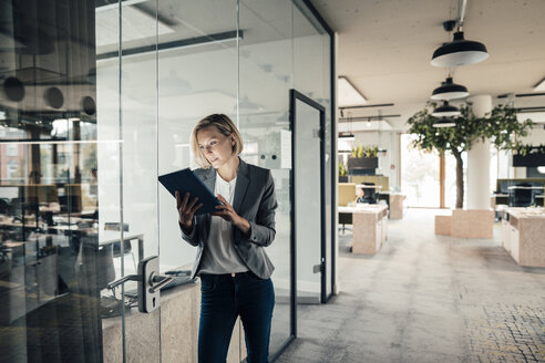 Female entrepreneur using digital tablet while leaning on glass wall - JOSEF04796