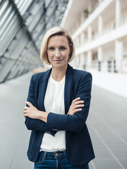 Confident female entrepreneur with arms crossed standing at office lobby - JOSEF04799