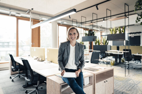 Lächelnde Geschäftsfrau mit digitalem Tablet auf dem Schreibtisch im Büro sitzend - JOSEF04800
