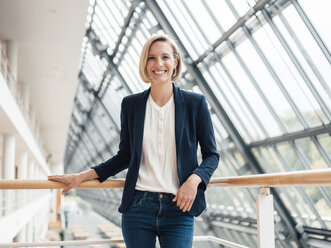 Businesswoman smiling while standing by railing in office - JOSEF04805