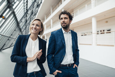 Businessman standing by smiling colleague at office lobby - JOSEF04810