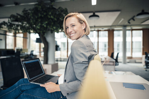 Lächelnde Geschäftsfrau mit Laptop auf dem Schreibtisch - JOSEF04826