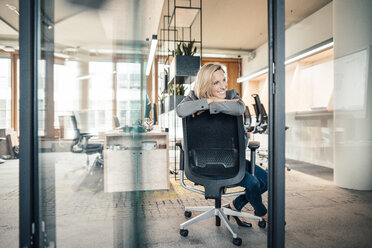 Female entrepreneur smiling while sitting on office chair - JOSEF04831