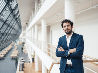 Confident male entrepreneur with arms crossed standing in office - JOSEF04837