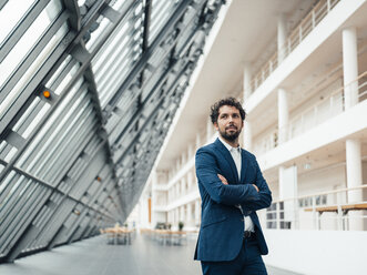 Businessman with arms crossed standing in office lobby - JOSEF04839