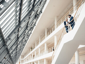 Male and female entrepreneur having discussion while standing in staircase - JOSEF04843