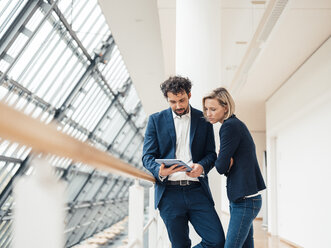 Professional team using digital tablet while standing at office corridor - JOSEF04844