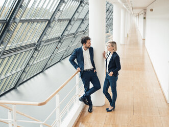 Male and female colleagues having discussion while standing at office corridor - JOSEF04850