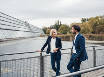 Female entrepreneur discussing with colleague while standing at office park - JOSEF04854